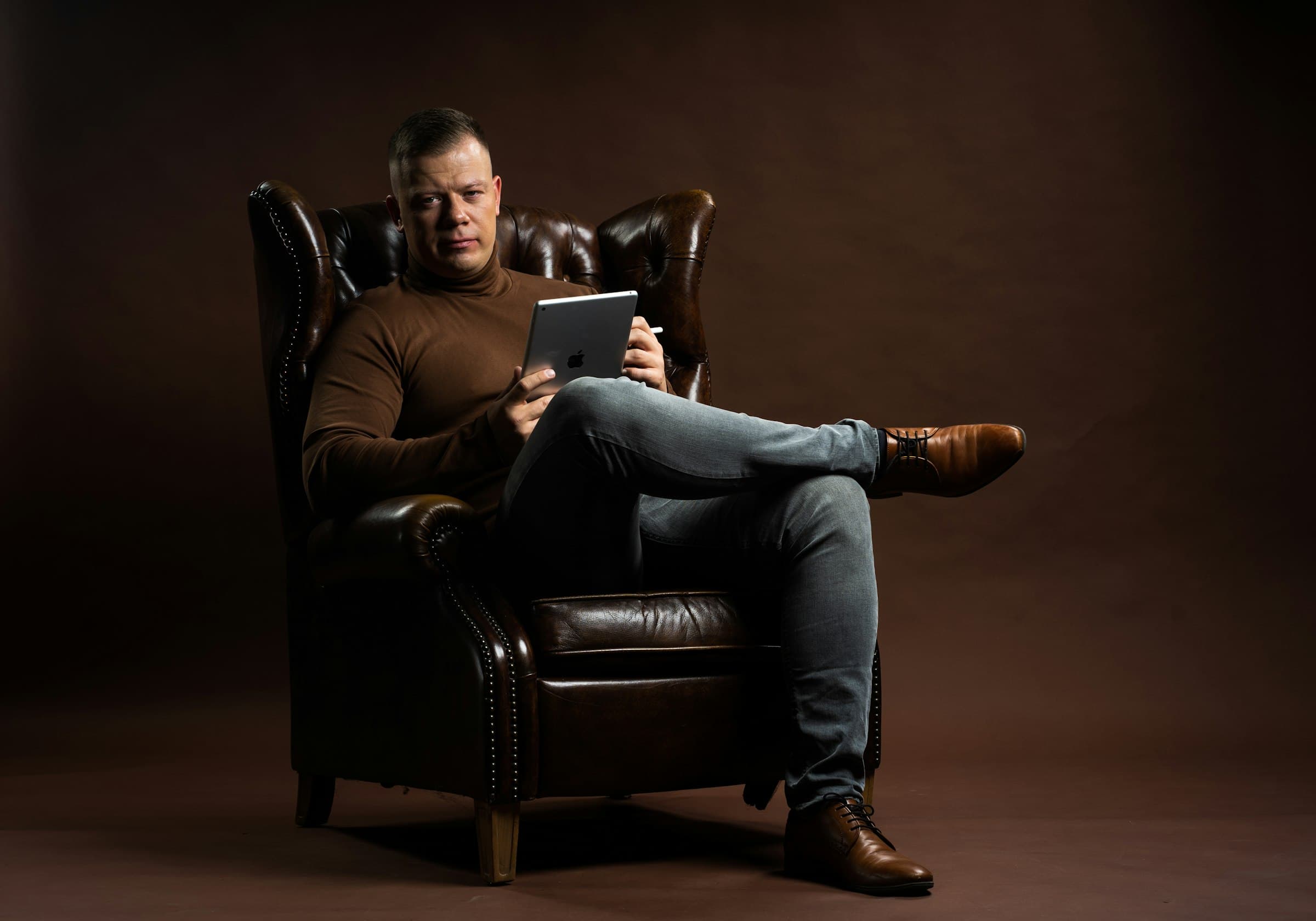 A man in a leather armchair reading on a tablet