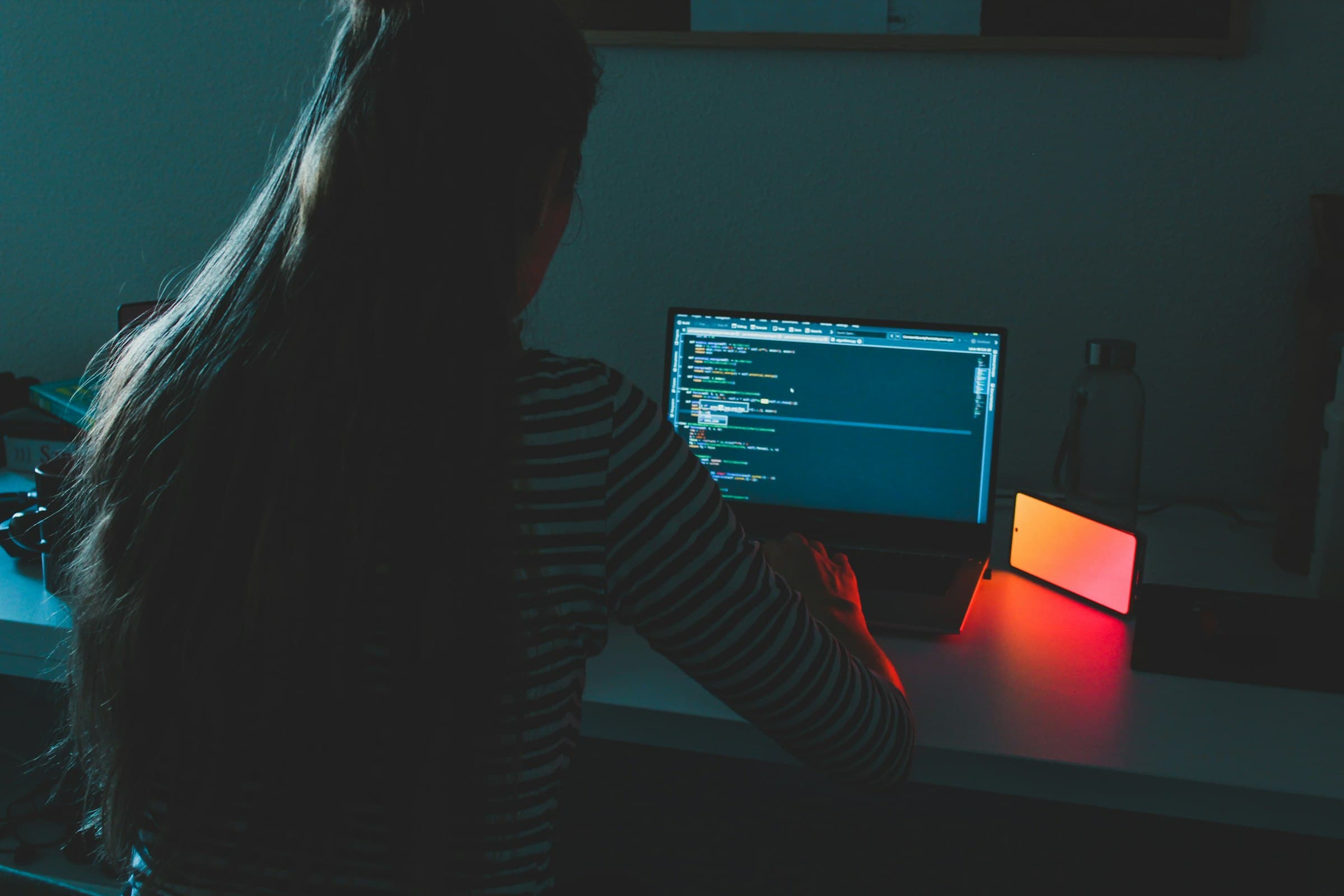 A woman writing code on a monitor in a dark room